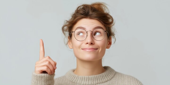 Woman smiling with a finger raised, suggesting a bright idea in casual attire against a light background.