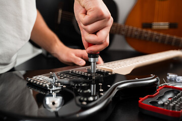 Adjusting Guitar Bridge with Screwdriver. Technician fine-tunes the chrome bridge of a black electric guitar with a screwdriver. Chrome bridge of the electric guitar is tightened with a screwdriver.