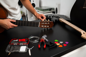 Guitar tuning process includes adjusting pegs and preparing new strings for better sound. Guitar string replacement and tuning preparation. Musician tunes a guitar using tools and spare strings.