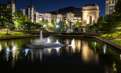 Illuminated arch monument in Atlanta at night with city buildings in background