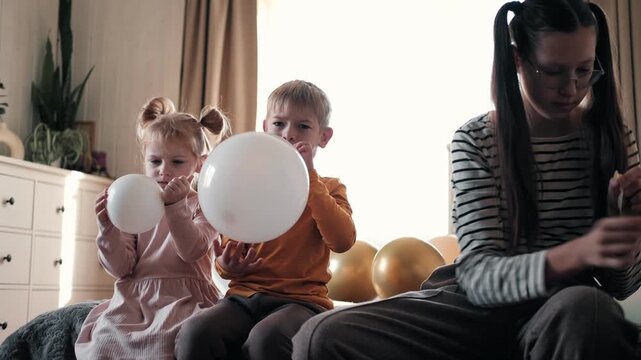 Family Fun Children Joyfully Blowing Up Balloons. Kids inflating balloons, prepare for birthday party. 3,6, 14 years old siblings racing blowing balloon, decorate the room. Bonding time together. Joy