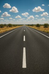 Fototapeta premium Endless asphalt highway under bright blue sky with drifting white clouds vanishing perspective and crisp lane markings capturing freedom of the open road and modern transport themes