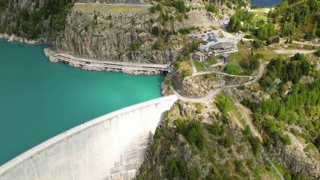 Aerial panoramic view of Emosson Dam in Finhaut, Switzerland, with turquoise lake, mountain station, parking area, and dramatic alpine scenery in the Swiss Alps.
