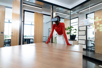 Fototapeta premium African American woman leaning on wooden conference table at office using VR headset, copy space
