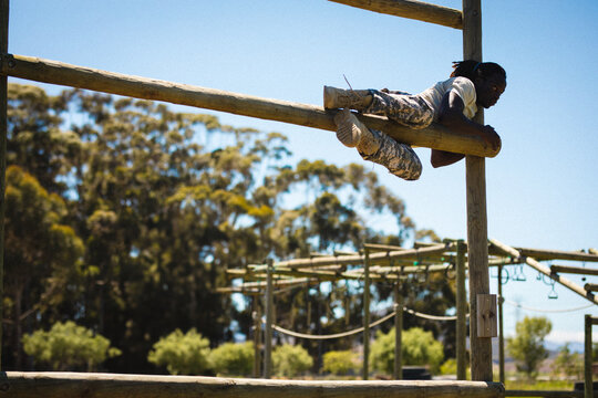 African American man climbing beam on outdoor course wearing camouflage pants, ropes, copy space