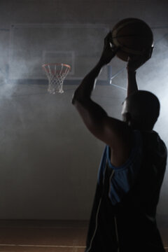 Fototapeta Basketball player hoisting basketball overhead on wooden court under dim haze, with strong shadows