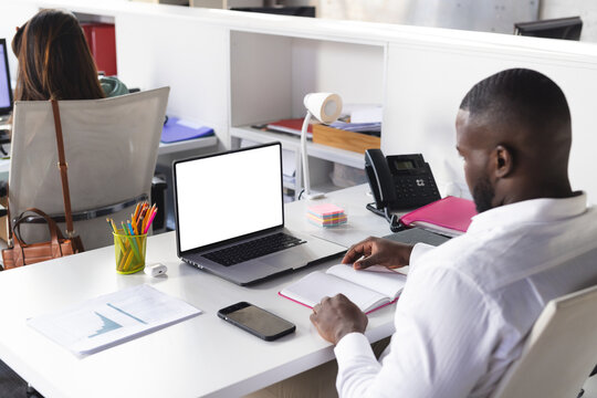 Diverse coworkers working at adjacent workstations in office with laptop and notebook, copy space - Powered by Adobe