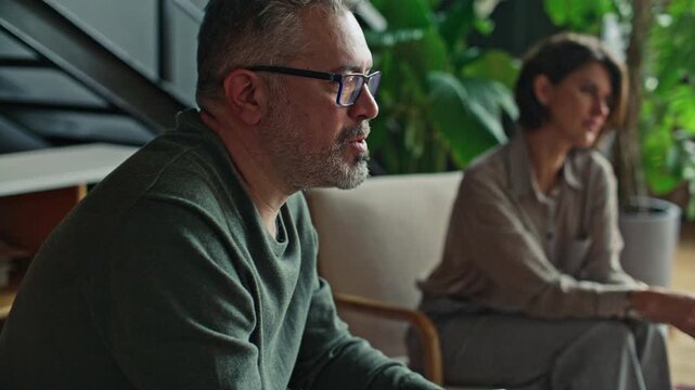 Middle-aged husband and wife sitting side by side in comfortable office and talking to psychologist during couple therapy session. Tilt-up shot, rack focus