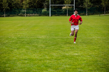 African American male athlete running across rugby pitch toward camera past goalposts, copy space