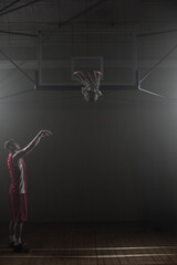 Basketball falling through net on wooden gym court under spotlights with deep shadows