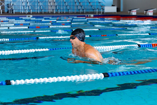 Male swimmer wearing cap and goggles gliding in breaststroke across lap pool toward starting blocks