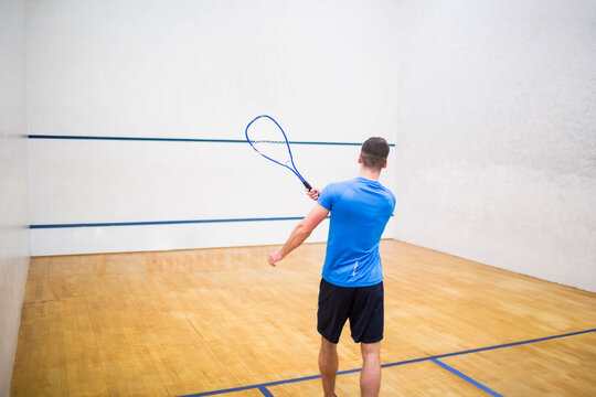 Fototapeta Squash player swinging racket on wooden floor, aiming shot against white wall marked by blue lines