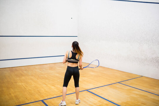 Fototapeta Squash player preparing to swing racket at ball on wooden court, blue lines and scuff marks