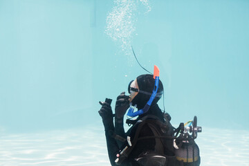 Scuba diver adjusting regulator while bubbles rising against clear turquoise training pool floor