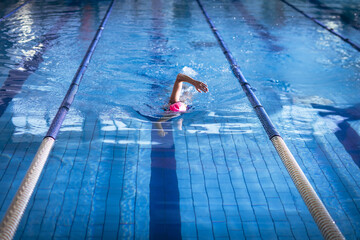 Senior female swimmer gliding through tiled pool lane by lane ropes in pink swim cap goggles