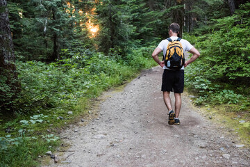 Male hiker pausing on dirt trail carrying yellow and black backpack with attached water bottle