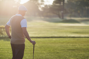 Senior Chinese man standing on verdant fairway at dawn wearing golf attire, gripping golf club