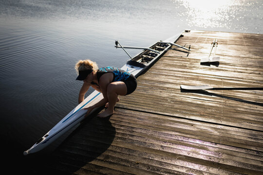 Woman wearing patterned tank top and visor guiding scull onto water at wooden dock, copy space - Powered by Adobe