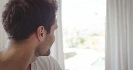 Man is wearing T-shirt and standing near glass door framed by white curtains, facing bright pool