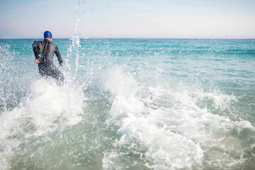 Male athlete striding into turquoise sea wearing neoprene wetsuit and blue swim cap, copy space