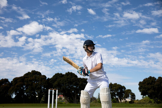 Adult male cricketer wearing helmet standing on green cricket field holding wooden bat, copy space