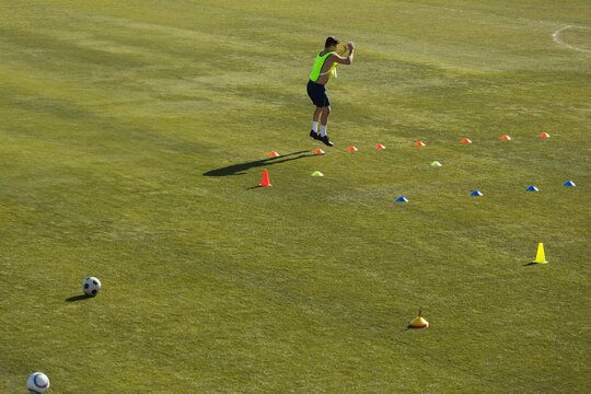 Male athlete wearing vest doing plyometric drill on field with cones and soccer ball, copy space