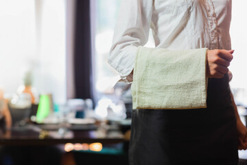 Waffle-weave cloth towel draping over black waist apron in restaurant dining area, with set tables