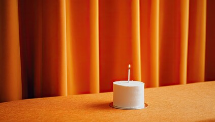 Small white cake with a lit candle against orange drapes