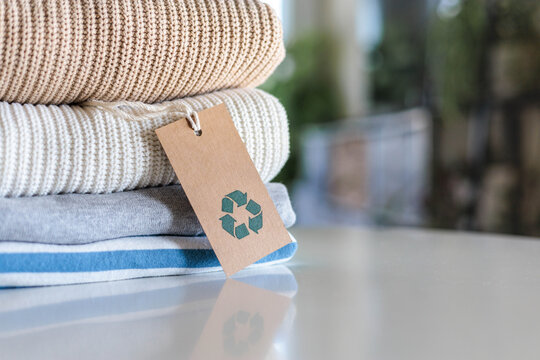 Knitted warm clothes neatly folded heap with craft tag recycling material circle arrow closeup