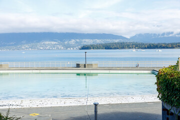 Scenic view of Kitsilano Pool with swimmers enjoying the water, framed by a serene waterfront, distant mountains, and a partly cloudy sky