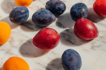 variety of plums and apricots on marble table