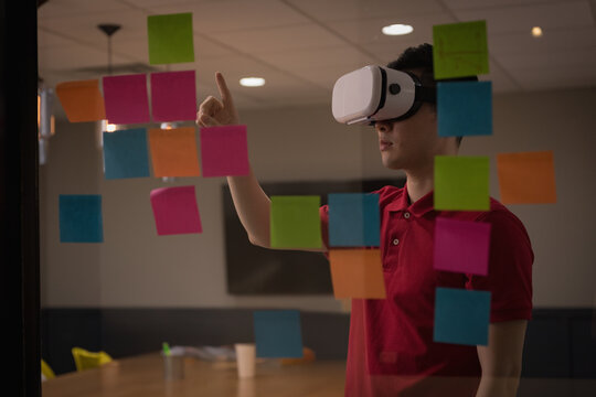 Asian man interacting with sticky notes through VR headset on panel in conference room, copy space