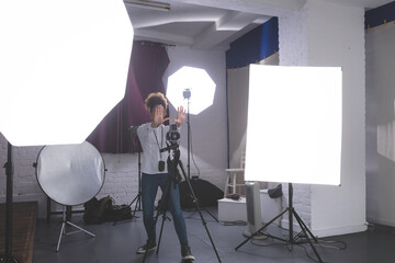 African American female photographer operating camera in studio with softbox light and reflector