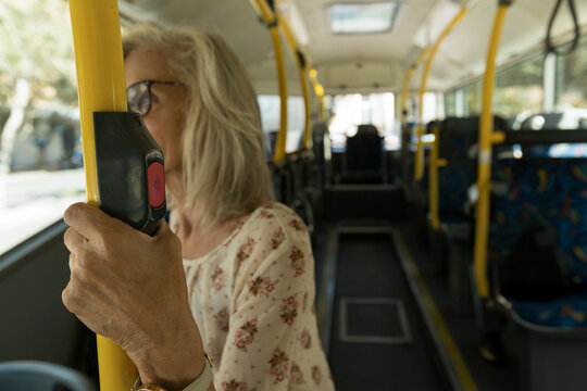 Senior woman with floral blouse holding yellow handrail pressing red button on city bus copy space