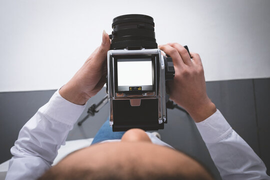 Female photographer wearing shirt using medium-format camera focusing screen with tripod in studio