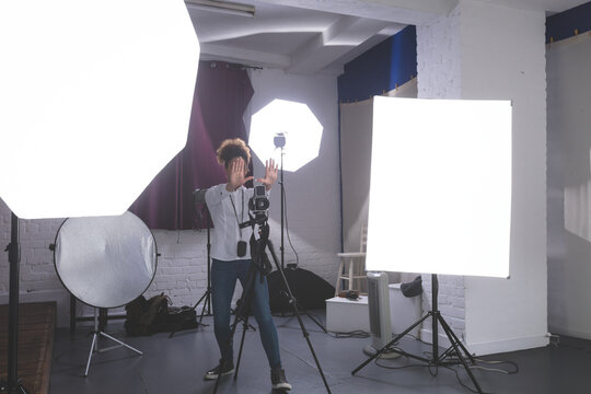 African American female photographer operating camera in studio with softbox light and reflector