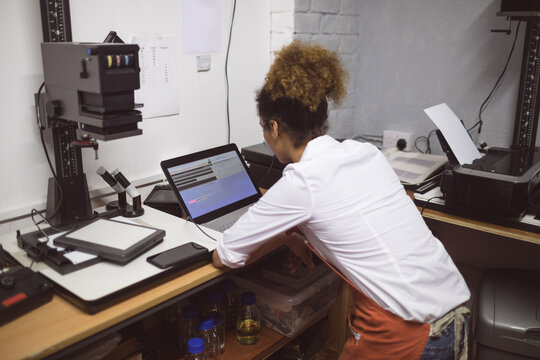 Female technician leaning over workbench in lab workspace using scanner and enlarger, copy space