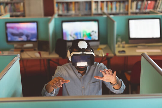 Adult Asian man wearing VR headset and interacting with virtual interface at library cubicle desk - Powered by Adobe