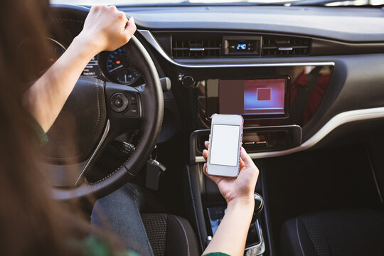Female driver gripping wheel while holding smartphone near gear shift lever inside car with key fob