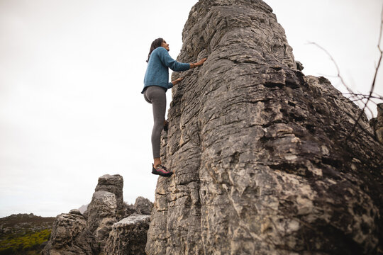 Female climber climbing limestone pillar wearing athletic clothing climbing shoes on rocky terrain