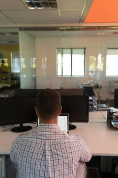 Male office worker sitting at white desk focusing on laptop between two monitors in modern office