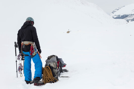 Standing male mountaineer on left snow slope carrying backpack and coiled rope, copy space
