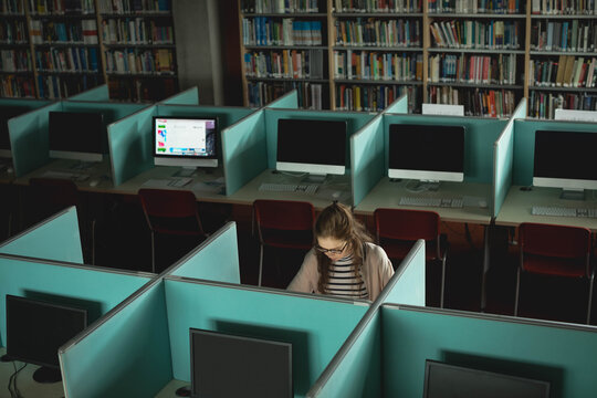 Female teenager studying at study cubicle in library lab using desktop computer keyboard and mouse