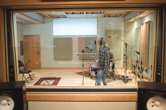 Female musician performing vocals at microphone stand in recording studio with drum kit behind