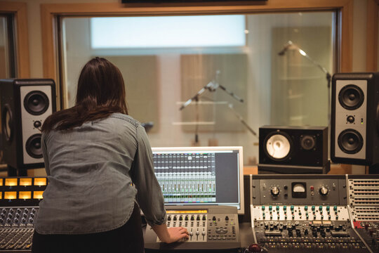 Female sound engineer adjusting faders and speakers, monitoring computer interface in control room