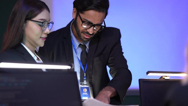 Two data analysts, a man and a woman, review technical specifications for a new software project, pointing at key metrics on a report during a late-night strategy session.