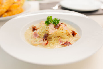 spaghetti carbonara on white dish, Creamy pasta carbonara with bacon bits and fresh parsley garnish served in white bowl. Classic Italian cuisine dish with rich sauce and herbs for dinner.
