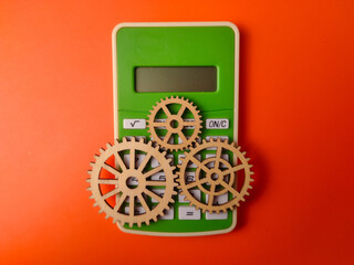 Top view green calculator accompanied by three wooden gears on an orange background