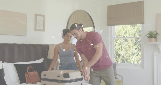 Couple placing hard-shell suitcase onto bed starting trip packing, organizing purses and wallets