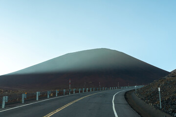 Sunset view from the summit of Mauna Kea on the Big Island of Hawaii, with volcanic slopes and clouds glowing in golden light.